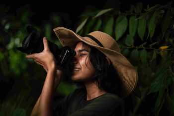 A lady wildlife photographer intently capturing images with a DSLR camera in a dense forest setting